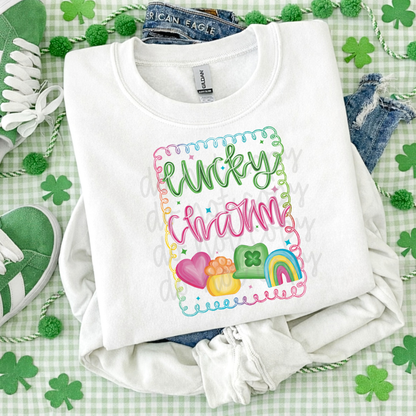 Lucky Charm St. Patrick’s Day graphic tee with colorful script lettering, heart, pot of gold, shamrock hat, and rainbow design on white Bella Canvas or Comfort Colors shirt.