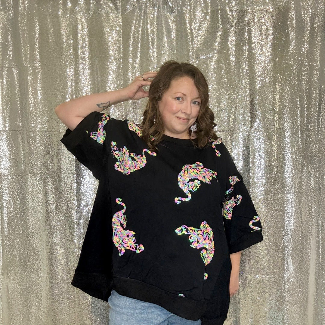 Person wearing a black top with colorful animal designs against a silver sequin backdrop