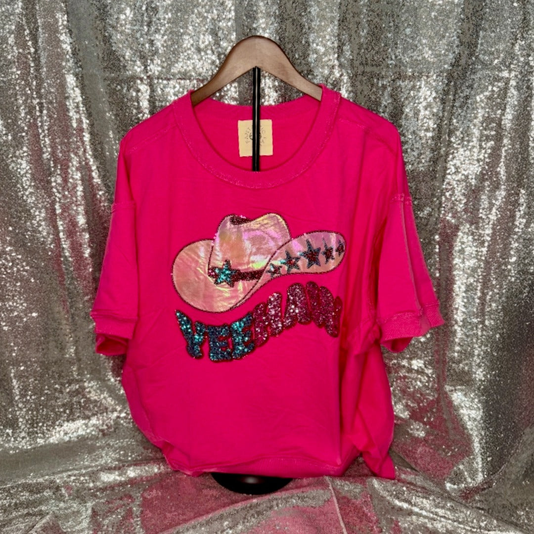 Pink top with sequin cowboy hat design on a hanger against a glittery silver background