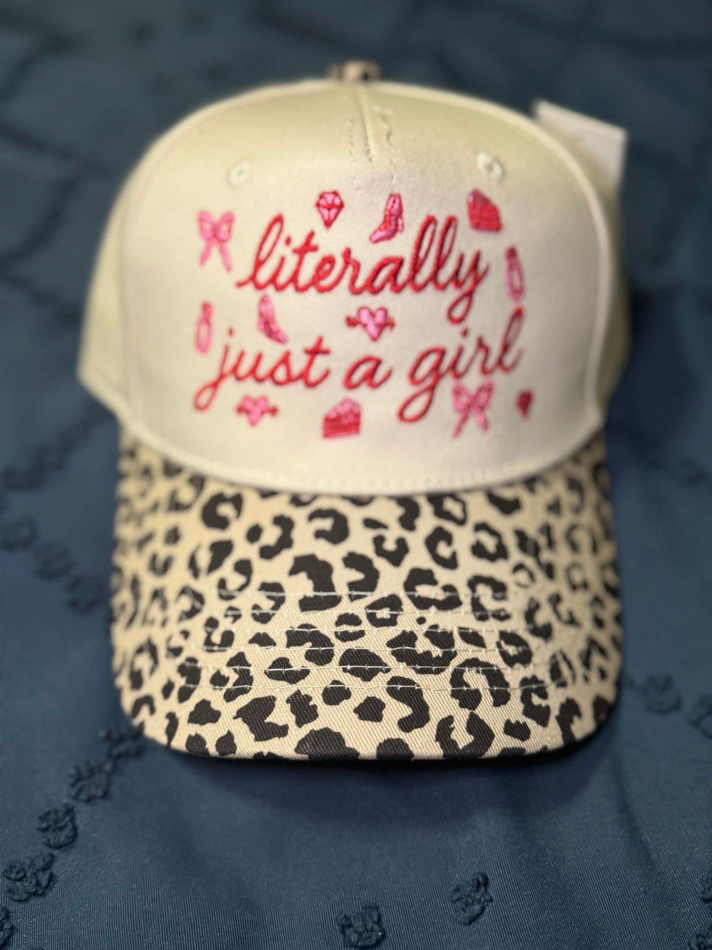 Hat with 'literally just a girl' text in red and leopard print brim on a blue textured background