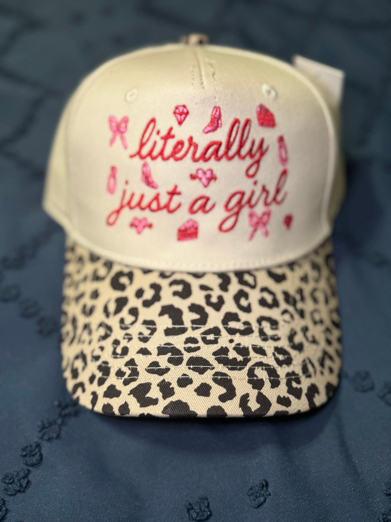 Hat with 'literally just a girl' text in red and leopard print brim on a blue textured background